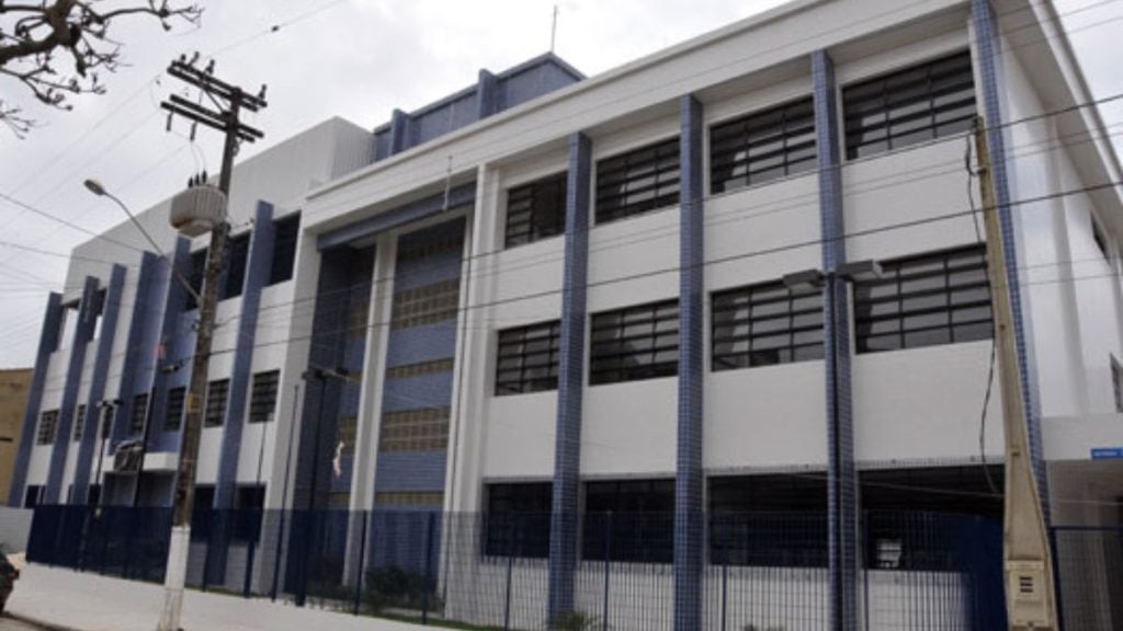 Fachada de uma escola pública com janelas e grades, em Praia Grande, SP, ilustrando o caso de menina agredida por colega e retorno às aulas sem apoio, segundo a mãe.
