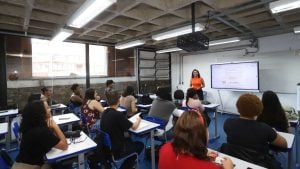 Sala de aula com alunos sentados em carteiras e uma instrutora apresentando conteúdo em lousa e telão, ilustrando vagas ceprocamp em cursos gratuitos de qualificação em Campinas.