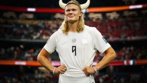 Erling Haaland em partida de futebol, usando uniforme branco da seleção norueguesa e a numeração 9, em estádio com arquibancadas ao fundo. Foto para redes sociais de Haaland