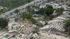 Vista aérea de área devastada por terremotos na Venezuela, com escombros de prédios, ruas com carros parados e filas de veículos ao lado de um complexo residencial, destacando a tragédia e os danos após o sismo.