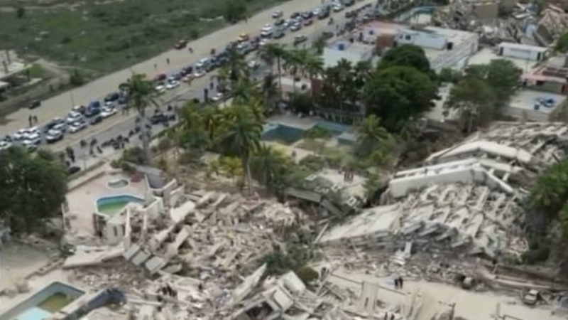 Vista aérea de área devastada por terremotos na Venezuela, com escombros de prédios, ruas com carros parados e filas de veículos ao lado de um complexo residencial, destacando a tragédia e os danos após o sismo.