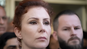 Carla Zambelli em foto de imprensa, em meio a um ambiente interno com outras pessoas ao fundo, em contexto de notícia sobre extradição na Itália.