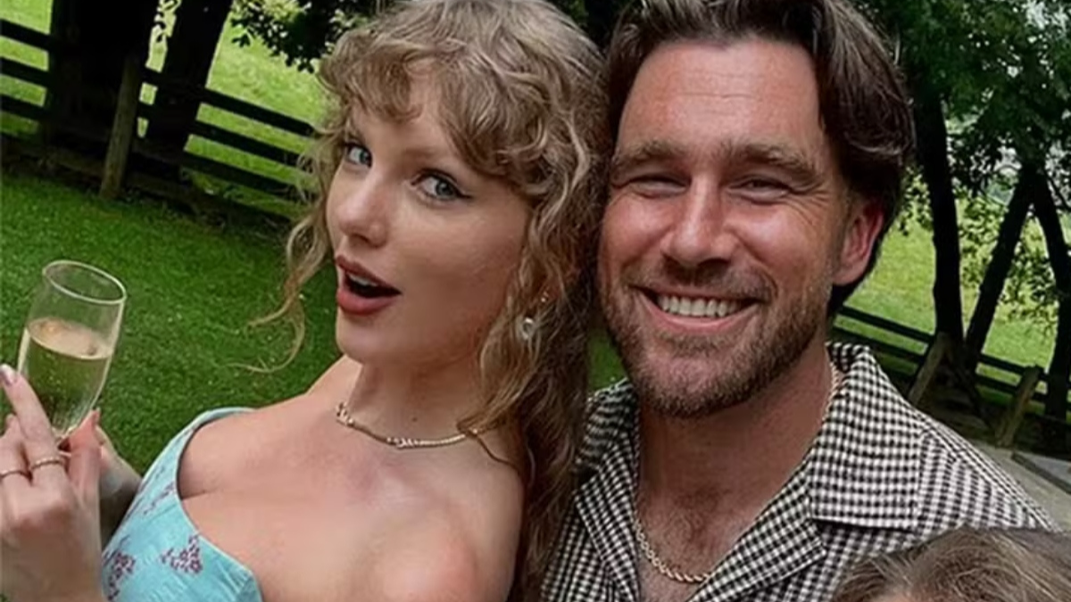 Taylor Swift e Travis Kelce posam juntos ao ar livre em um cenário verde, com Taylor em vestido azul e Travis sorrindo ao lado dela, em clima de celebração.