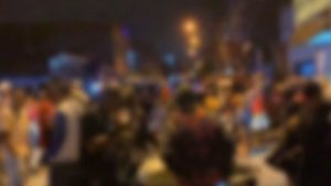 Festa agitada com multidão em rua à noite, em São Vicente, durante baile funk encerrado pela PM após confusão com pedras e álcool.