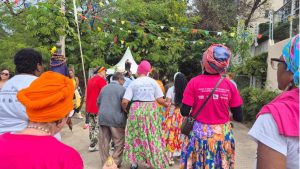 Pessoas caminham em uma rua decorada com bandeirolas coloridas durante o Arraial Afro Julino, em Campinas, com participantes usando roupas e camisetas do evento