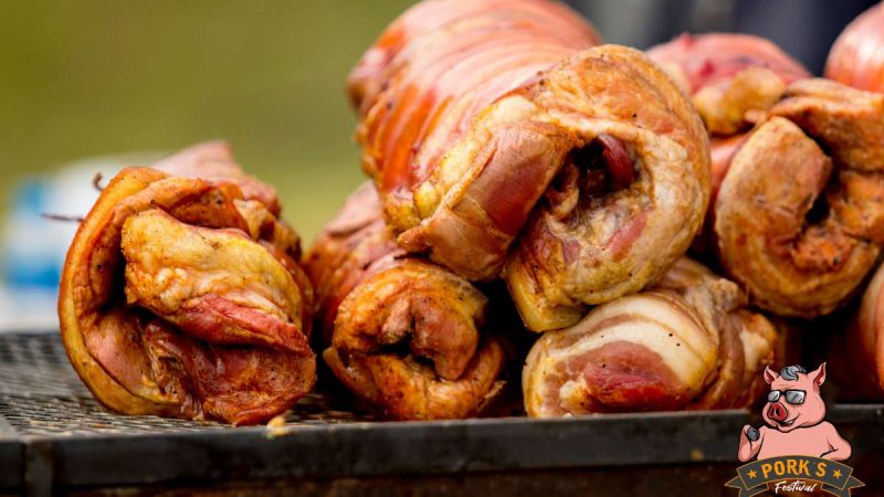 Pork's Festival em 9 de julho: carnes suínas assadas com pele crocante em destaque sobre uma bancada, sugerindo a gastronomia do evento com entrada gratuita e clima de rock.