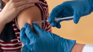 Profissional de saúde com luvas azuis prepara seringa com agulha para aplicar a Vacina contra HPV em uma pessoa em atendimento clínico, reforçando a campanha prorrogada em Campinas.