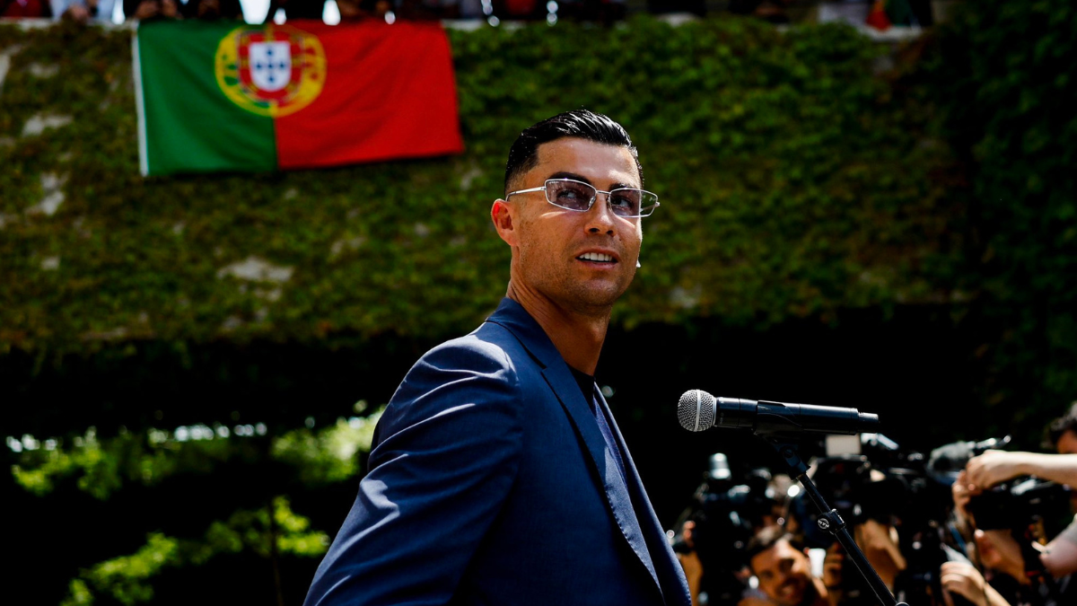 Cristiano Ronaldo em evento de imprensa, posando ao lado de microfones e câmeras, com bandeira de Portugal ao fundo, em contexto de declaração sobre a última Copa.