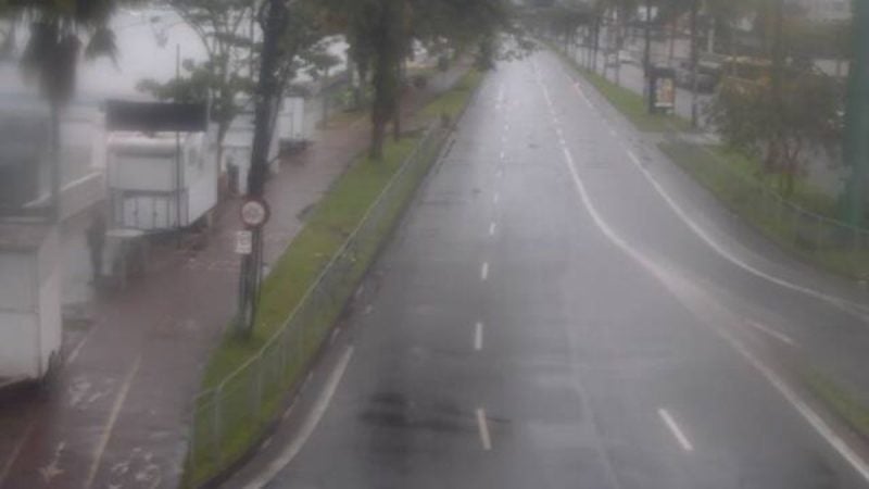 Chuva intensa causa alagamentos na Baixada Santista, com rua alagada e água cobrindo a pista em meio ao tráfego, mostrando estragos e vias comprometidas.