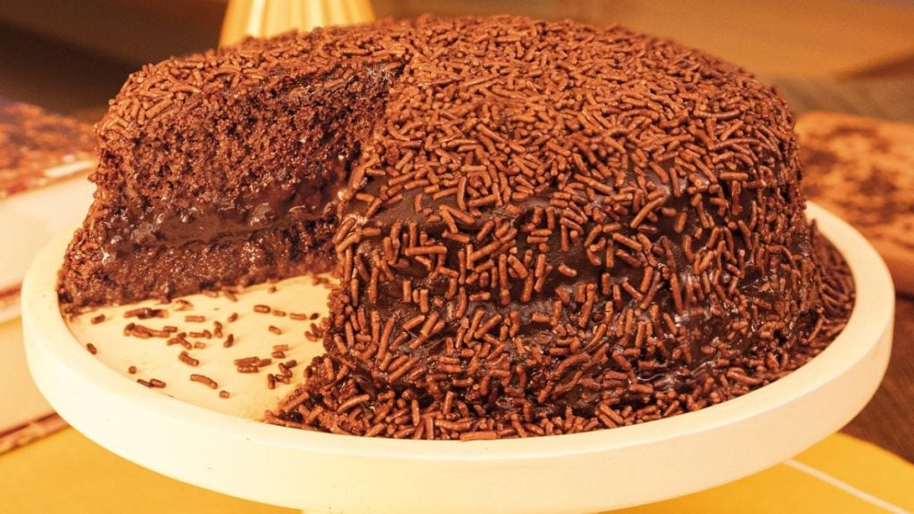 Bolo de chocolate coberto com granulado escuro em um prato branco, com textura cremosa e detalhes bem destacados, imagem ideal para o Dia do Chocolate.
