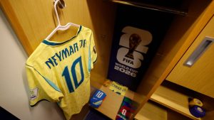 Camiseta amarela do time do Neymar com o número 10 e a marca Nfymar, ao lado de troféu e objetos do FIFA World Cup 2026, em ambiente de vestiário.