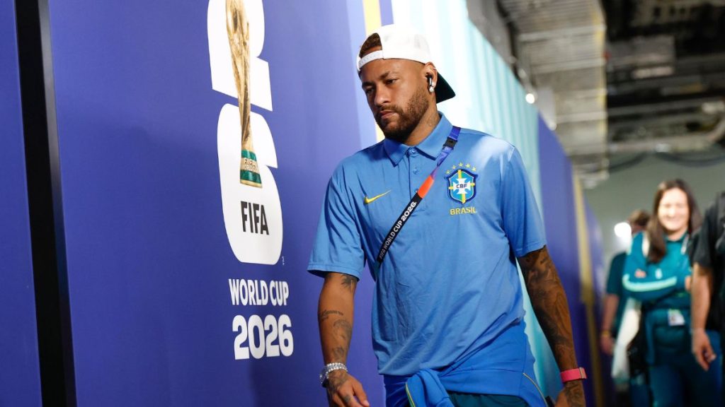 Neymar com a camisa da Seleção Brasileira e fone de ouvido no estádio durante evento da Copa do Mundo, ao lado de banner “World Cup 2026”, em clima de possível encerramento de ciclo.