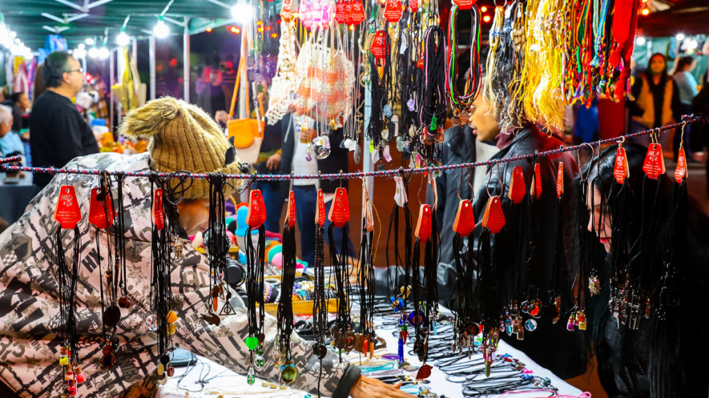 Feira com produtos artesanais no Espaço de Economia Criativa durante o Festival Gastronômico de Inverno: acessórios e peças coloridas em expositores sob iluminação festiva, com pessoas circulando ao fundo.