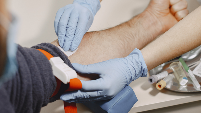 Campanha de doação de sangue Santa Bárbara d’Oeste: profissional com luvas esteriliza e realiza coleta de sangue em um doador, mostrando as mãos e o procedimento em bancada clínica.