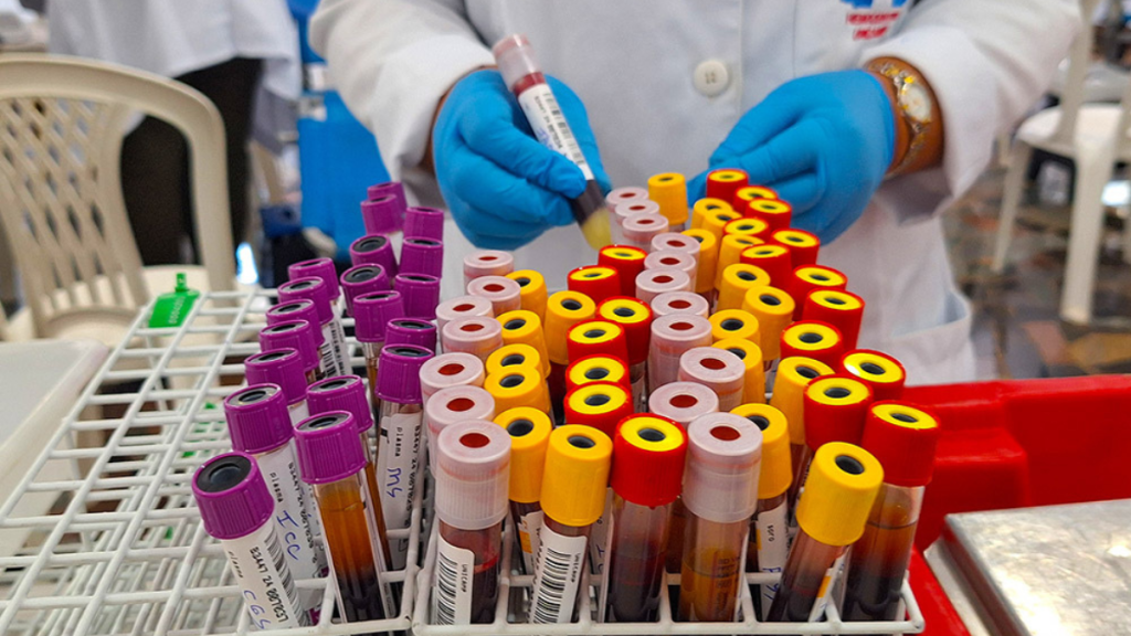 Doação de sangue Santa Bárbara d’Oeste: profissional de saúde com luvas prepara tubos de coleta em laboratório, com amostras etiquetadas para triagem e doação. Crédito: Prefeitura de Santa Bárbara D’Oeste.