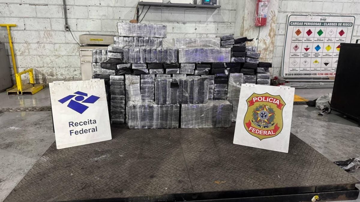Apreensão de drogas no Porto de Santos: caixas e pacotes com tabletes de cocaína enfileirados em um galpão da Receita Federal, com placas da Polícia Federal e Receita Federal ao fundo.