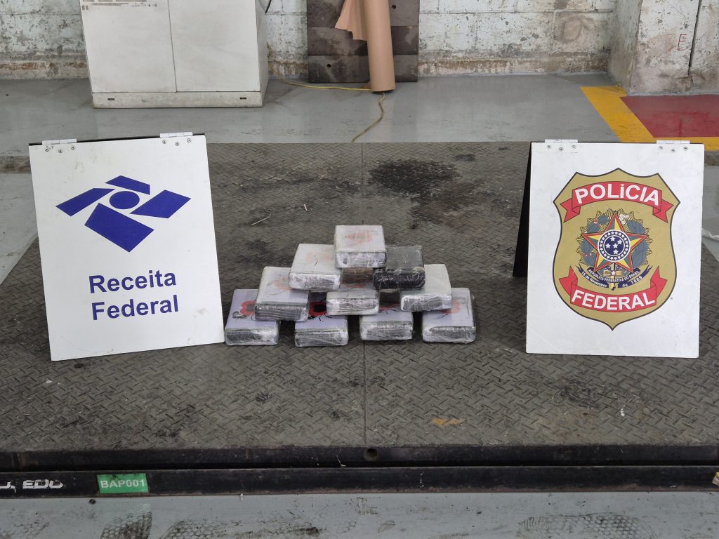 Apreensão da Receita Federal: tablets e blocos de cocaína embalados ao lado de placas da Receita Federal e da Polícia Federal, em operação no Porto de Santos.