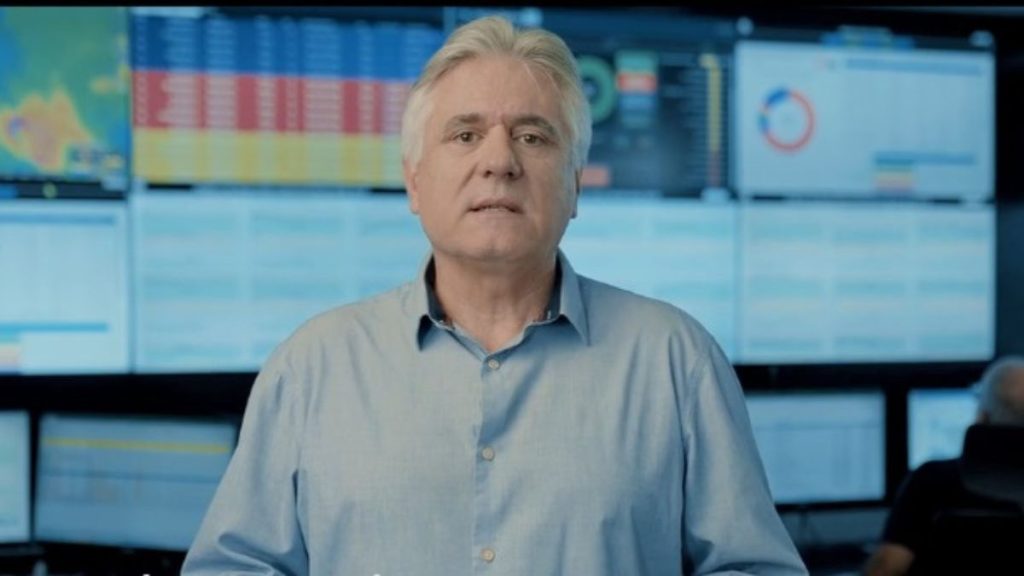 Gerente da Sabesp fala em vídeo sobre investimentos da Sabesp na Baixada Santista, com gráficos e painéis ao fundo, destacando maior segurança hídrica.