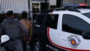 Homem detido próximo a uma viatura da Polícia Militar, com vítima ao fundo, em cena de tentativa de roubo de motocicleta em Atibaia, com agressão com faca.