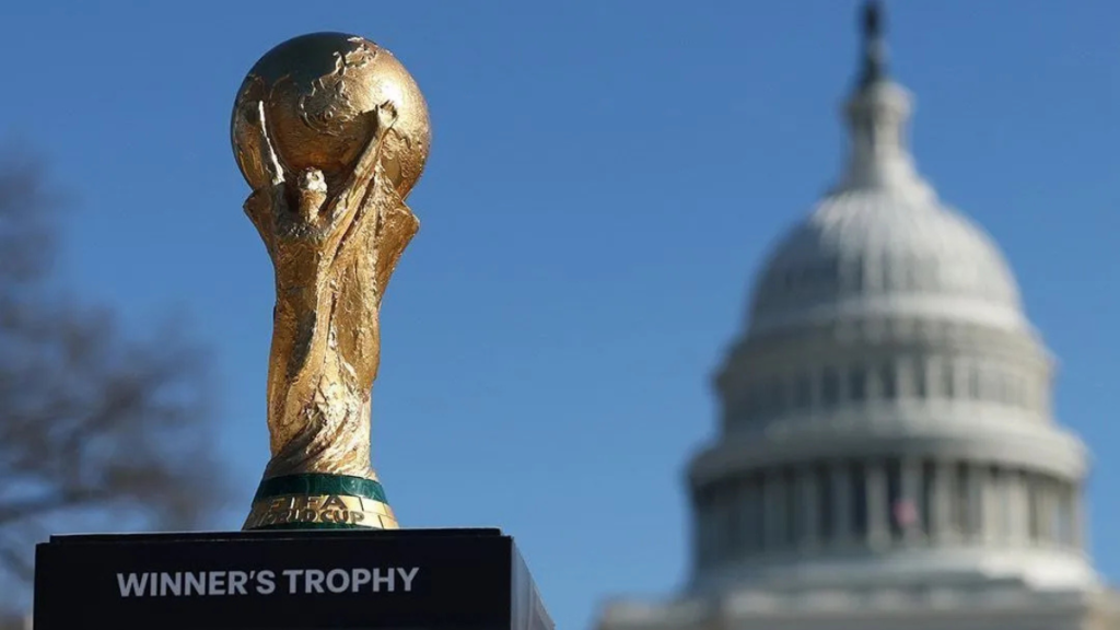 Taça dourada de campeonato em primeiro plano com o fundo desfocado do Capitólio ao céu azul, imagem usada para acompanhar as quartas de final da Copa do Mundo 2026 e o chaveamento até a final.