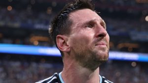 Messi em campo durante jogo da Copa, com expressão séria e frustrada, olhando para o lado enquanto a torcida ao fundo desfoca, destacando o momento negativo.
