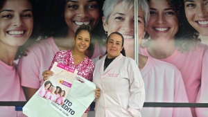 Ônibus da Mamografia oferece exames gratuitos sem agendamento em Guarujá, com equipe em destaque e material da campanha ao lado de mulheres em uniforme rosa.