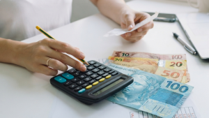 Cálculo de valores trabalhistas com calculadora e cédulas de dinheiro sobre uma mesa, representando a penhora de salário em dívida trabalhista pelo TST.