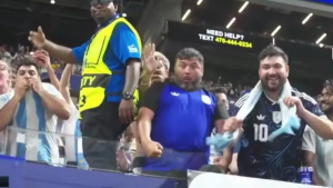 IShowSpeed em estádio de futebol, com torcedores argentinos ao fundo, após denúncia de racismo na partida da Argentina contra o Egito. O influencer aparece acenando, enquanto a torcida celebra.