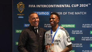 Youri Djorkaeff, sorrindo ao lado de um jogador, recebe troféu em cerimônia do FIFA Intercontinental Cup 2024, em backdrop com logos e faixa de melhor jogador.