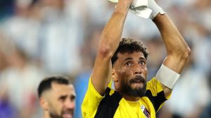 Vozinha em destaque nas negociações, com jogador em campo erguendo o troféu, braços levantados e expressão de comemoração em imagem esportiva com camisa amarela e preta.