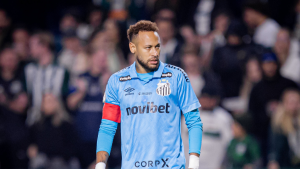 Neymar Santos em campo usando o uniforme do Santos Futebol Clube durante partida, com expressão focada e arquibancada desfocada ao fundo.