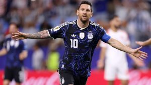 Argentina em partida de futebol: Lionel Messi com a camisa azul e preta da seleção argentina, número 10, fazendo gesto com os braços abertos no estádio, em clima de semifinal contra a Inglaterra.