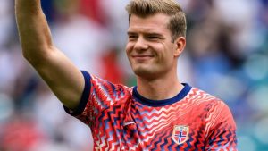 Sorloth em campo, usando a camisa da seleção da Noruega com padrão vermelho e azul, com o braço erguido, comemorando após eliminação da Noruega para a Inglaterra na Copa e recebendo ameaças.