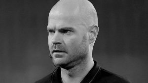 Retrato em preto e branco do árbitro Rob Dieperink, com microfone de headset no rosto, em imagem de notícia sobre sua morte aos 38 anos.