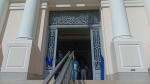 Entrada de novo hospital em Campinas, com colunas brancas e portão ornamentado, bandeiras ao fundo e pessoas atravessando a escada durante a inauguração