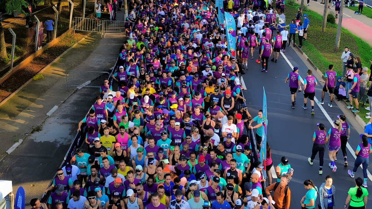 Multidão de corredores na pista durante a Maratona de Campinas, com participantes usando camisetas coloridas e bandeiras ao longo do percurso da 9ª edição. A Maratona de Campinas 2026 está chegando.