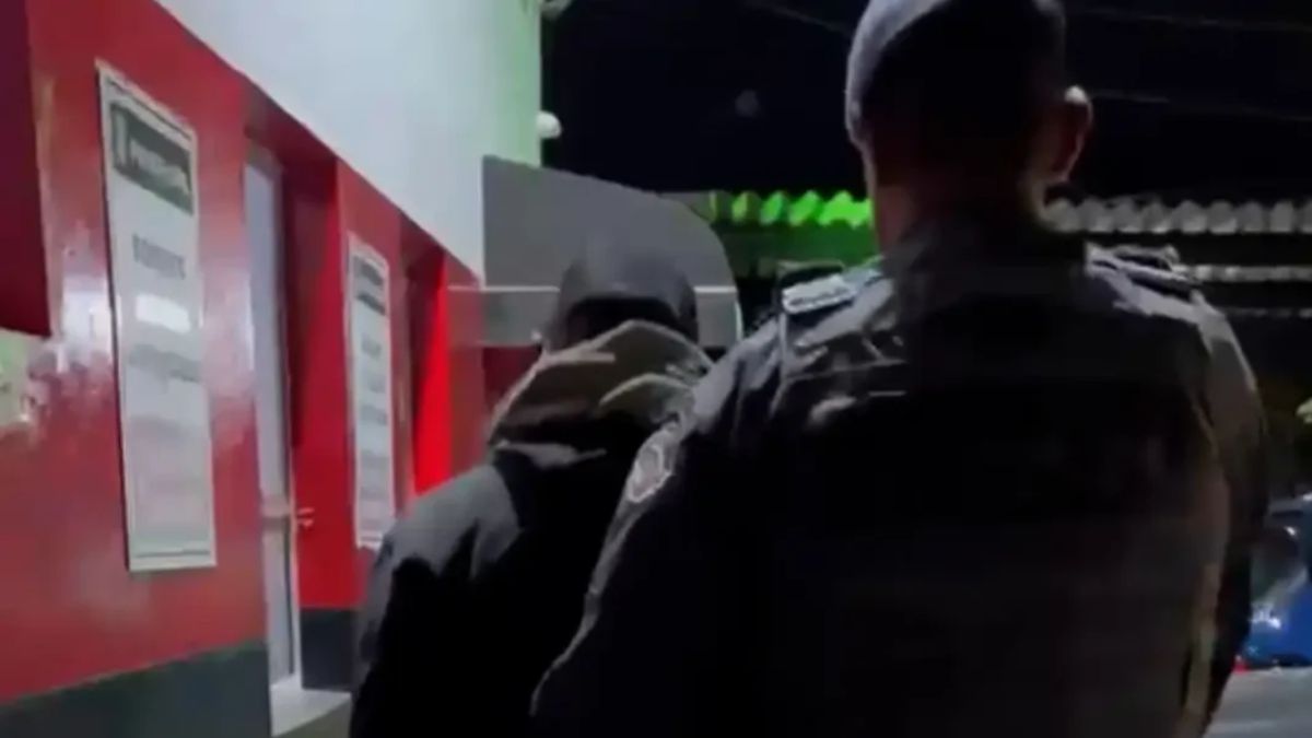 Policial em frente a uma viatura vermelha e uma porta de delegacia, em cena noturna que ilustra a prisão de motorista sem CNH em Bragança após oferecer R$ 1 mil a agentes.