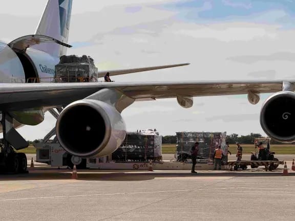 Avião de carga no aeroporto com caixas e equipamentos de logística em pista, ao lado de seis aeronaves usadas na operação para os shows de Harry Styles em SP, com foco em Viracopos.