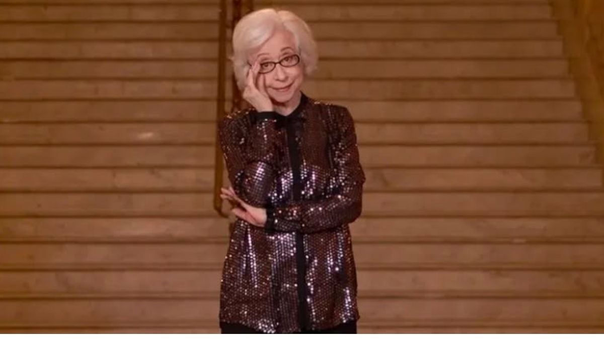 Fernanda Montenegro em evento, em pé e sorrindo, vestindo roupa escura com brilho, fazendo um alerta sobre uso de sua imagem em golpe: “É um crime”.