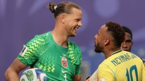 Ørjan Nyland, goleiro da Noruega, em uniforme verde, sorrindo durante partida com Neymar, em cena de gesto e conversa no campo.