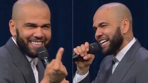 Daniel Alves aparece em evento religioso, sorrindo e segurando um microfone, em cena ao lado de painel com duas imagens. O ex-jogador gesticula durante a fala.