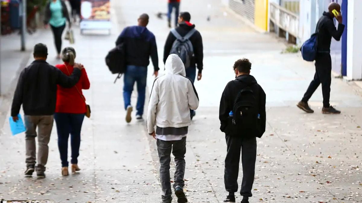 Pessoas caminhando na rua em dia frio, com roupas pesadas e capuzes, em alerta da Defesa Civil para frio intenso em SP entre hoje e quinta-feira.