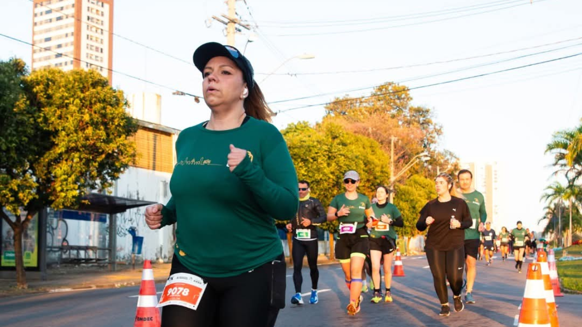Maratona de Campinas 2026: corredor em primeiro plano usando boné e camiseta verde corre em via urbana com cones de sinalização e outros atletas ao fundo em dia de prova.