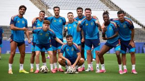Elenco da seleção da Espanha em treino, com jogadores usando uniforme azul, formando pose no gramado e bola no chão, remete à Espanha na Copa do Mundo