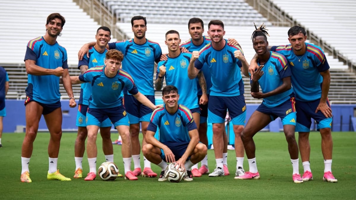 Elenco da seleção da Espanha em treino, com jogadores usando uniforme azul, formando pose no gramado e bola no chão, remete à Espanha na Copa do Mundo