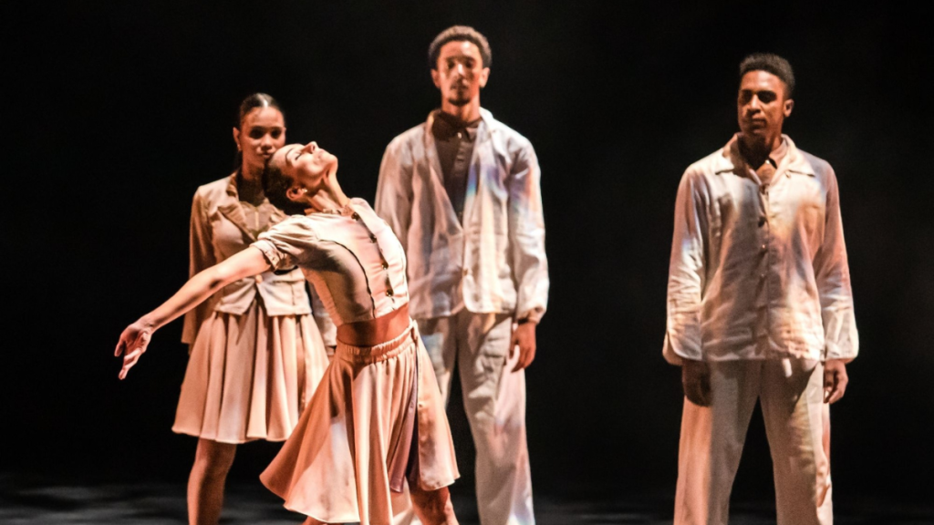 Cena de dança contemporânea da São Paulo Companhia de Dança em Santa Bárbara d’Oeste: bailarinos em cena com figurinos claros, um deles em destaque sendo carregado durante a obra Umbó.