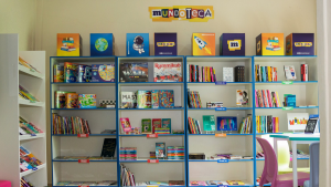 Acervo organizado da Mundoteca em Bragança Paulista, com prateleiras cheias de livros e jogos educativos ao fundo e espaço para leitura e brincadeiras