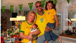 Lore Improta e família posam para foto em clima de comemoração, com a apresentadora segurando o filho recém-nascido, em ambiente decorado com bandeirinhas do Brasil.