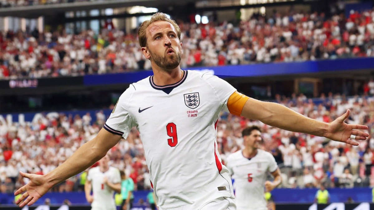 Harry Kane em partida de futebol com a camisa da Inglaterra, número 9, comemorando com os braços abertos em meio à torcida no estádio