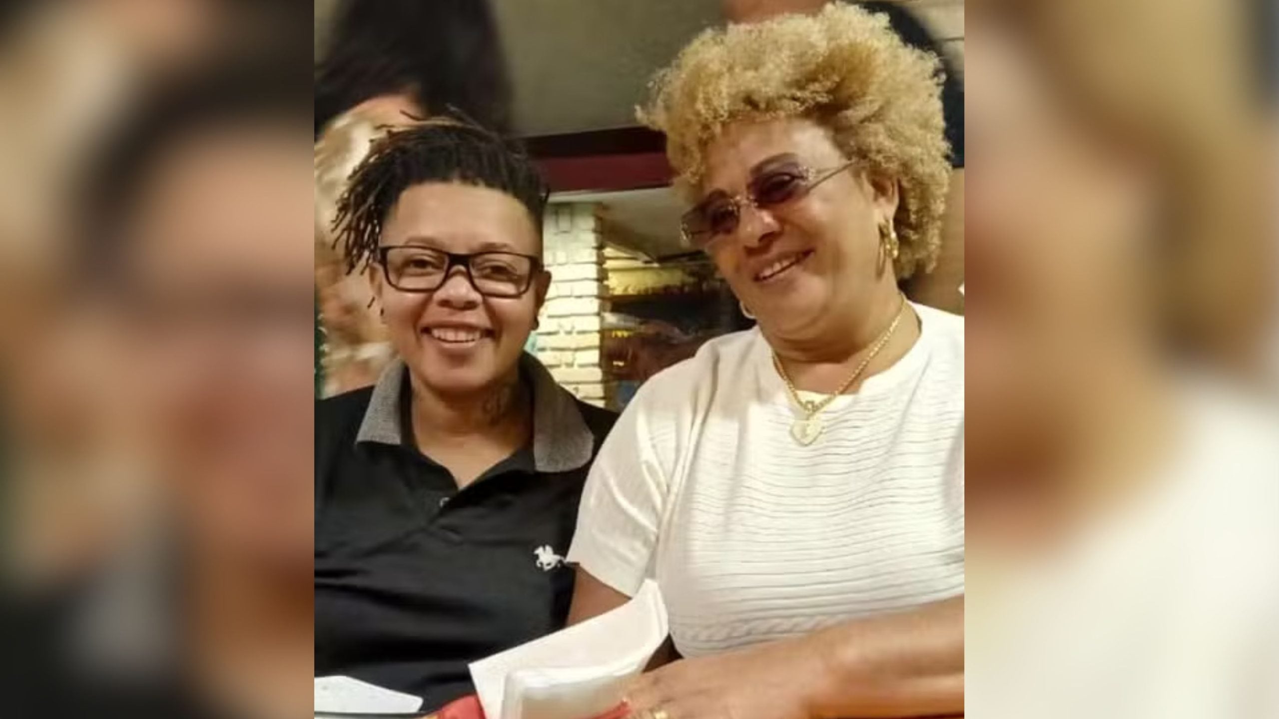 Casal sorridente em foto de arquivo, com mulher de cabelo curto e óculos e outra mulher com cabelo armado e acessório no pescoço, em contexto de investigação de desaparecimento em Praia Grande.